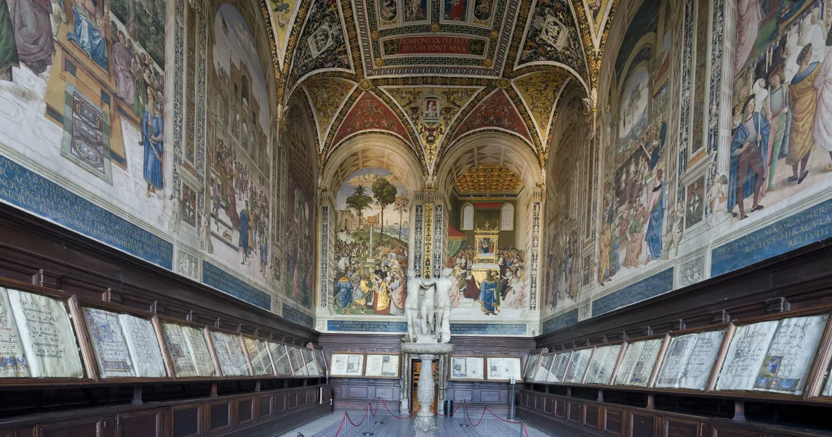 The Piccolomini Library inside Siena Cathedral, its walls and vault covered in bright Pinturicchio frescoes above wooden cases of choir books