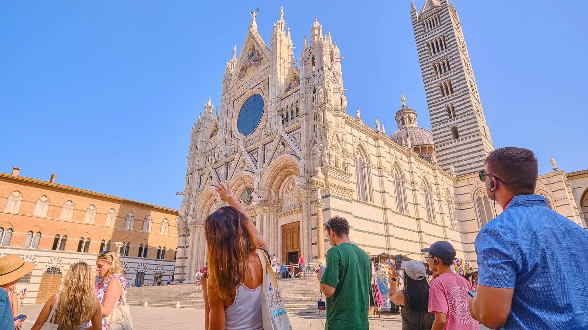 Visitors with a guide in front of the facade and bell tower of Siena Cathedral, from the three-town day trip listing
