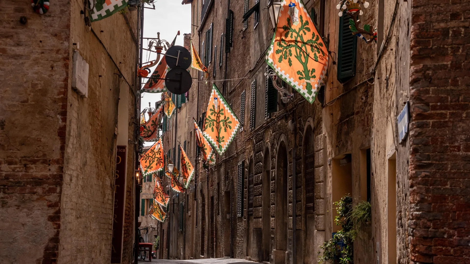A narrow medieval street in Siena hung with contrada flags, from the private walking tour listing