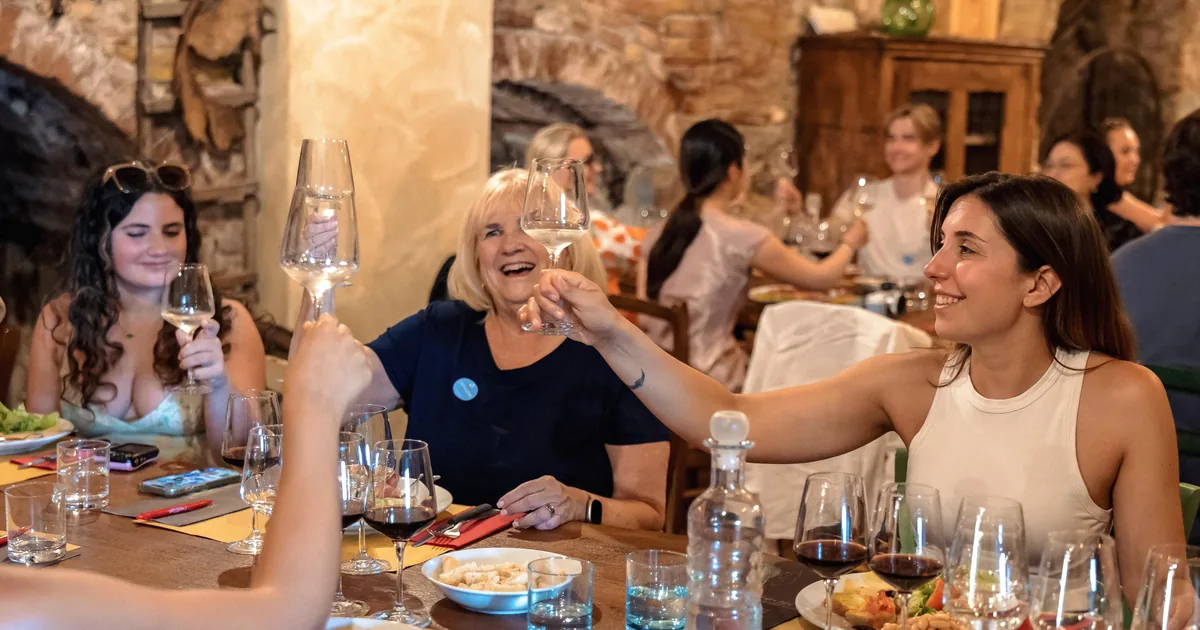 Guests raising glasses of red wine at a long table during a winery lunch in the Chianti hills